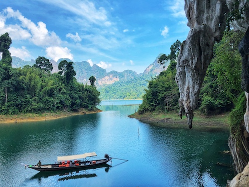 long tail boat floating on cheow lan lake with limestone cliffs in the background in khao sok