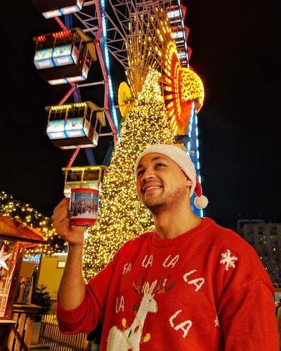 a man drinking glühwein in front of a ferris wheel at a german xmas market