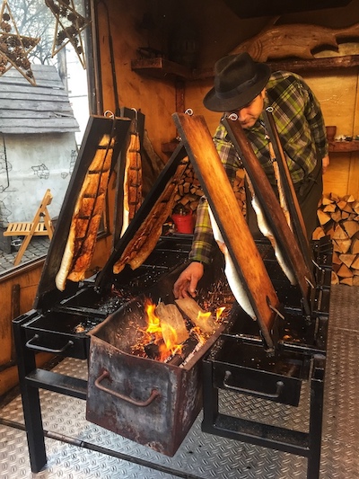 a man smoking fish on an open fire at spandau christmas market in germany