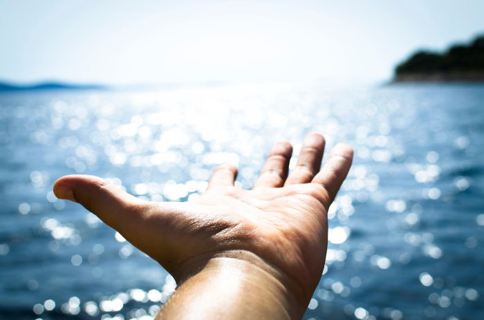 man stretching out his hand to the sun with a ocean in front