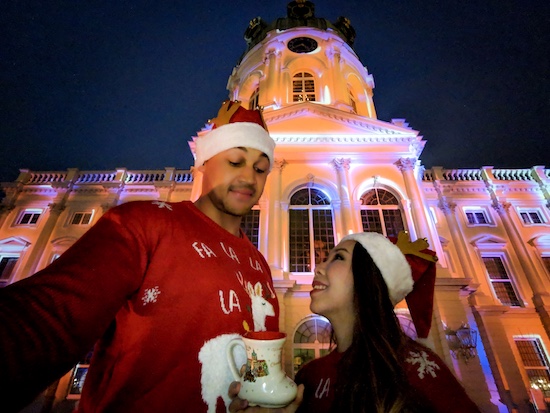 a couple wearing xmas jerseys standing in front of charlottenburg palace in berlin with the facades lit up in bright lights