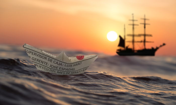 a paper boat floating on the ocean with a diving liveaboard in the background 