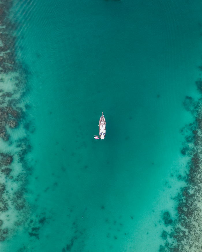 an aerial view of a scuba diving liveaboard from the sky in the middle of a turquoise ocean