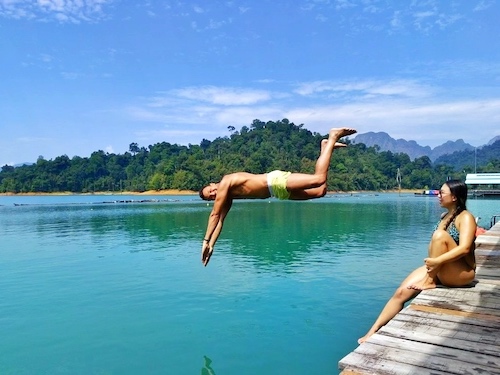 man jumping into cheow lan lake in thailand with woman watching