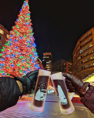 two people holding up xmas beer mugs with a christmas tree in the background