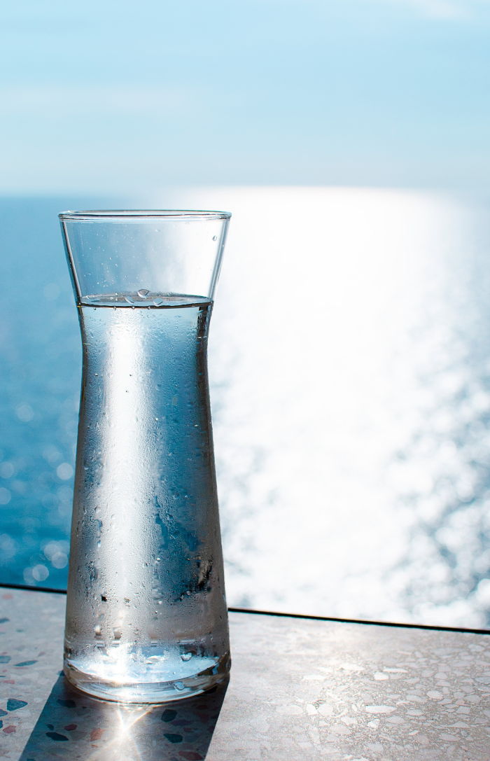 a carafe of water sitting on a table with a view of the ocean