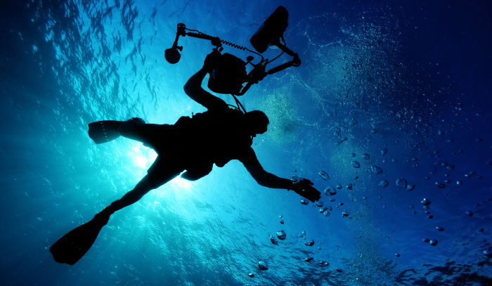 scuba diving beginner holding camera equipment close to the surface of the ocean