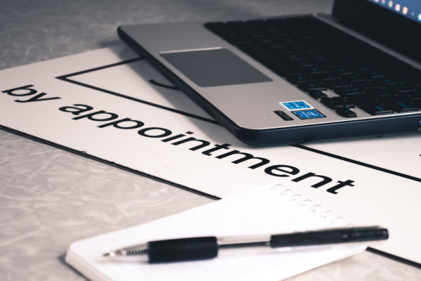 a laptop, pen and notebook place on a table and the words 'by appointment' printed on a large sheet of paper