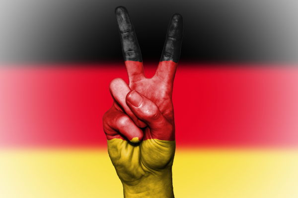 the Germany flag behind a hand painted in the Germany flag colours gesturing the piece symbol 