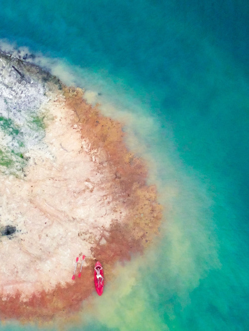 an aerial shot of man laying in a kayak perched on a clay island in Thailand