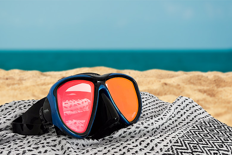 red tinted snorkel masks in blue with black silicon skirting lying on a towel on a beach