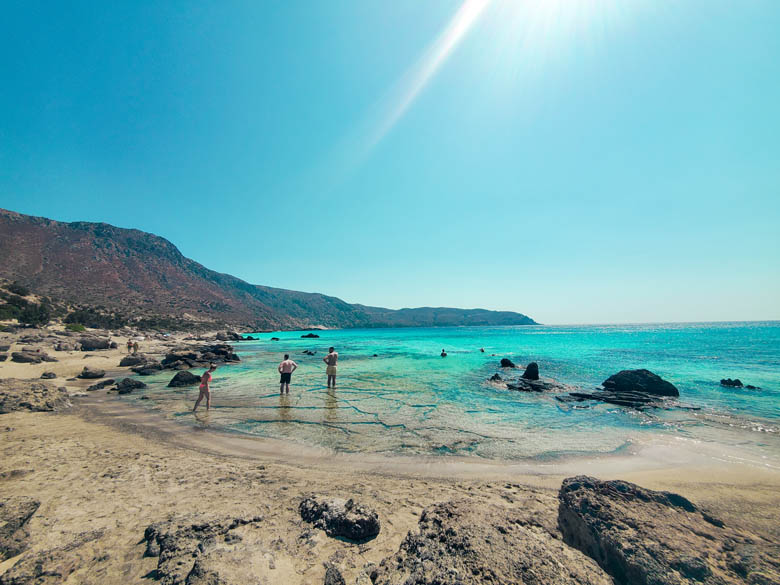 a few travelers standing in the shallow waters at kedrodasos beach with kids snorkeling in the crystal clear waters