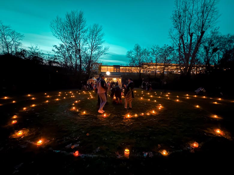 candles places in 4 concentric circles on the grass outside s prellerweg train station in berlin germany with people standing in the center