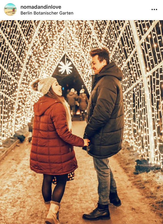 night photography of a couple walking down a tunnel of fairylights at berlin botanischer garten christmas market