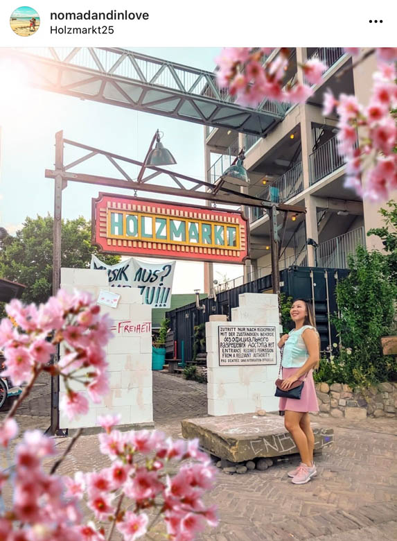 a woman standing in front of a popular flea market in berlin, holzmarkt with pink cherry blossoms framing the photo