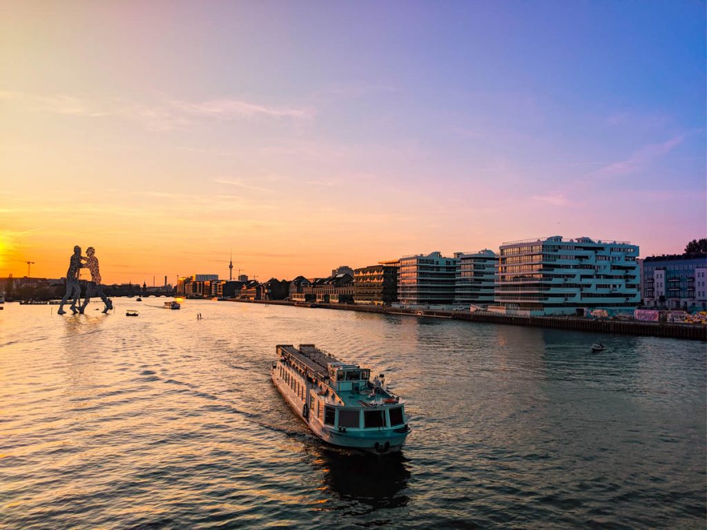 sun setting over the spree river with molecule man sculpture in the background - one of the pros of living in berlin