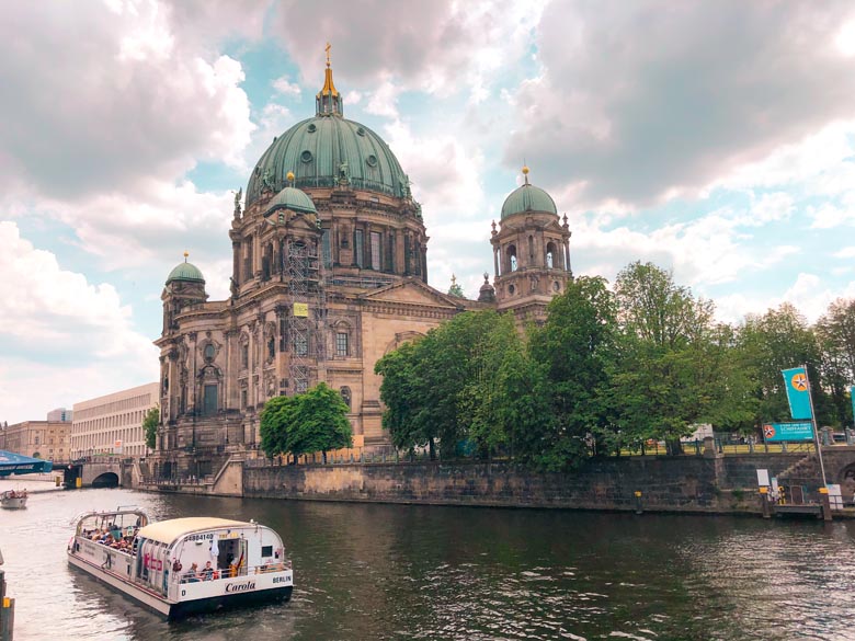 a view of the berlin cathedral and a boat with tourists sailing down the river in the city center