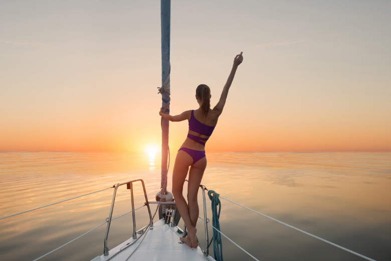 a woman standing on the bow of one of the best liveaboard boats while admiring the setting sun over the calm ocean