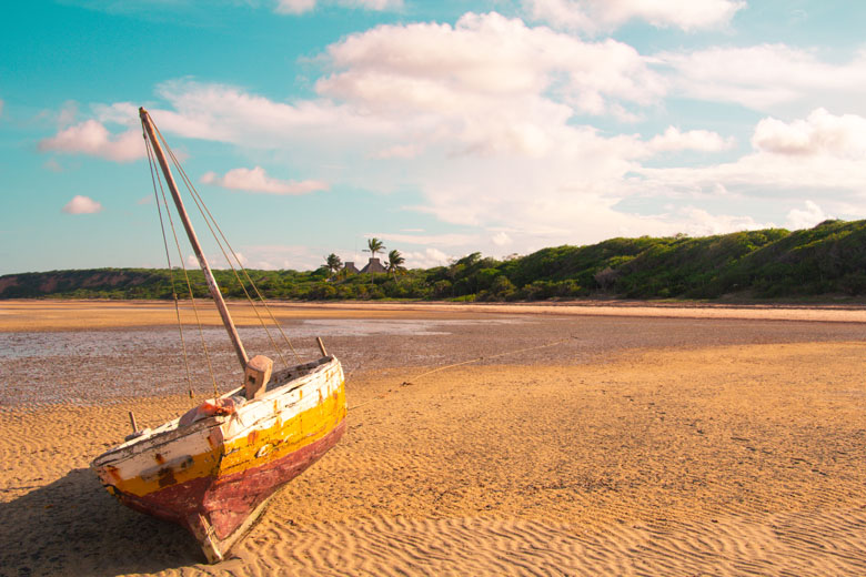 a wooden dhow aground on the receded shore in front of a beach resort in the far distance in Vilanculos Mozambique