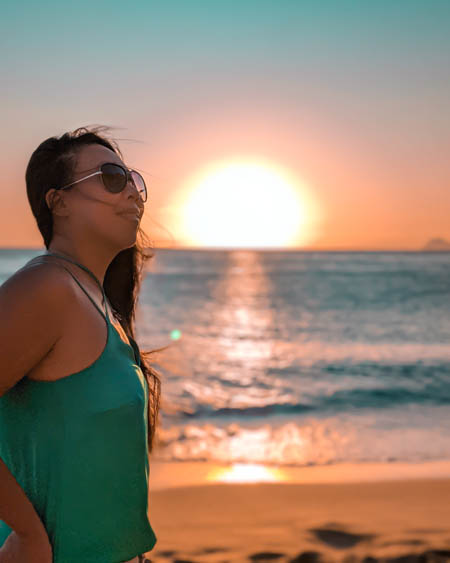 instagram photo of a woman standing on red beach in crete with the sun setting in the background