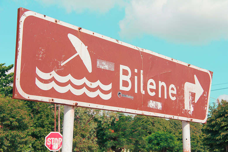 a road sign with a beach and umbrella on it pointing in the direction towards Bilene along the EN4 national road in Mozambique