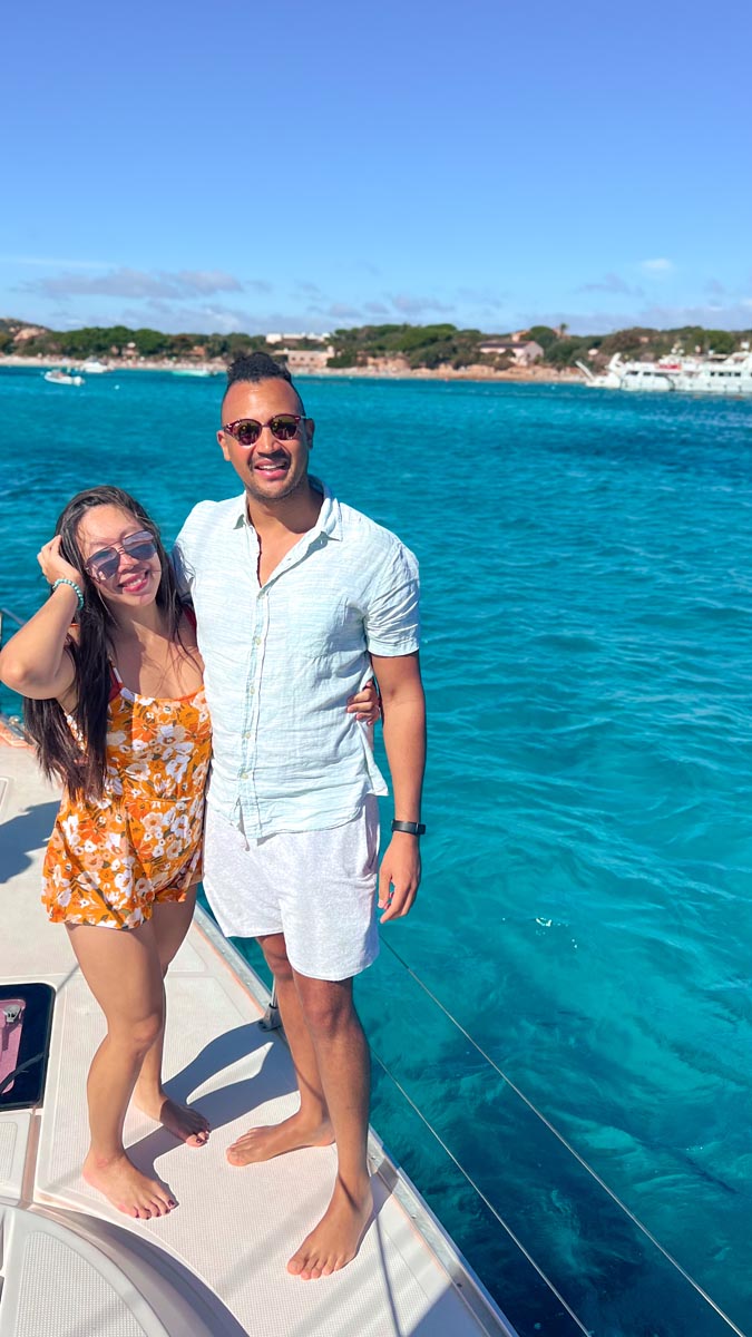 a couple standing on a sailing boat touring la maddelena islands with electric turquiose blue water in the background