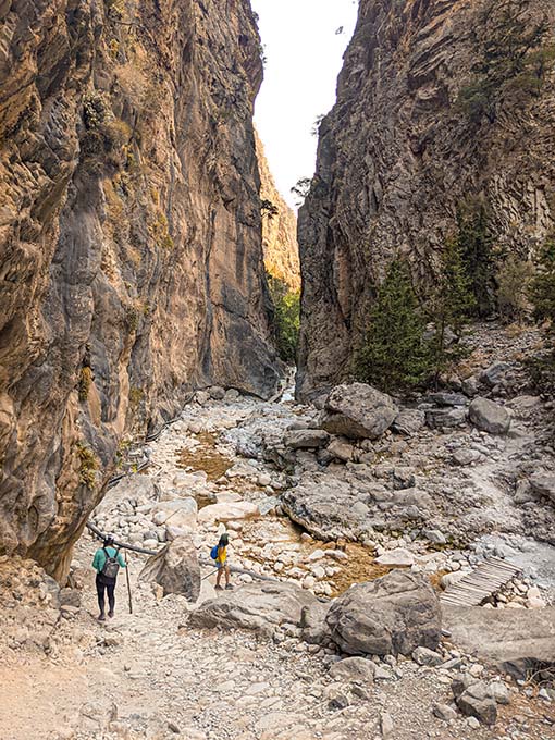 two women walking on a rocky trail at samaria gorge close to the narrowest section called the iron gates