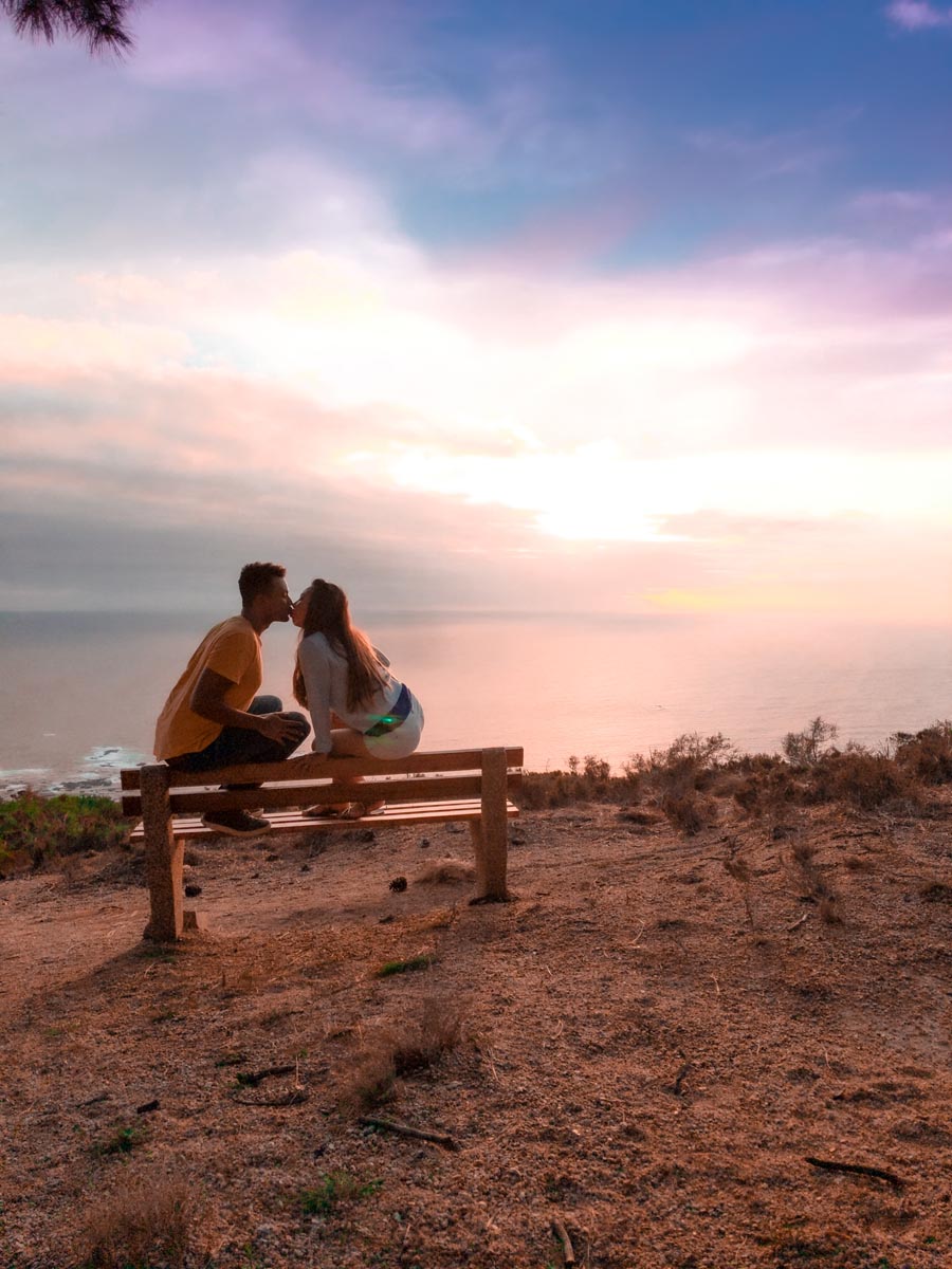 a couple kissing on a beach at signal hill with the sunset on the horizon overlooking the atlantic ocean