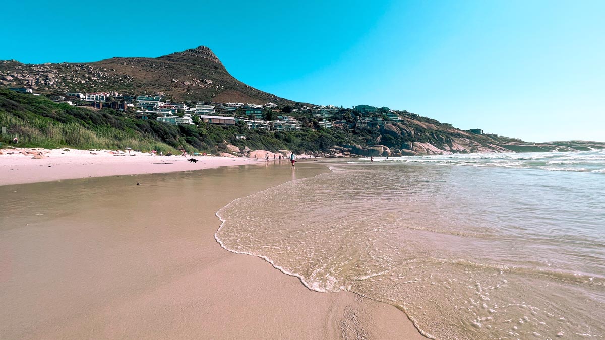 the clear waters of llandudno beach with white sand a few people and the mountain in the background