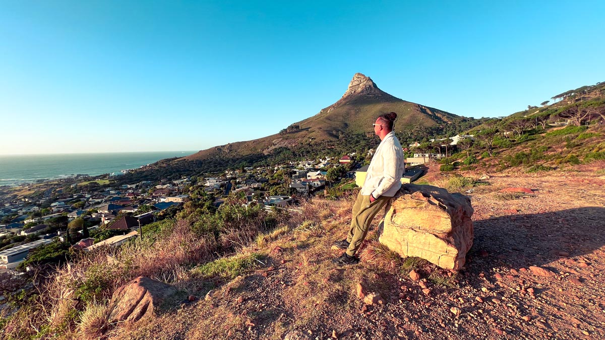 a man leaning against a rock with a view of signal hill and lion's head in the background