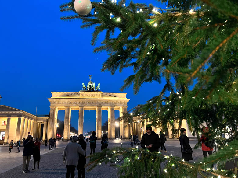 a view of brandenburg gate in berlin at blue hour with people standing on the square and a christmas tree