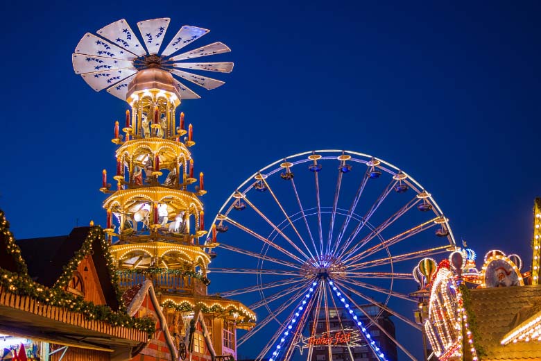 christmas market stalls, a giant ferris wheel and a traditional german christmas wooden pyramid or windmill at a xmas market in germany