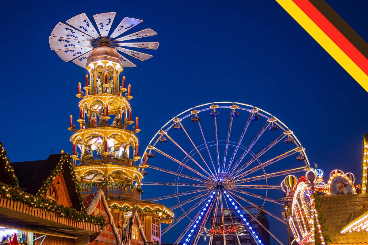 christmas market stalls, a giant ferris wheel and a traditional german christmas wooden pyramid or windmill at a xmas market in germany