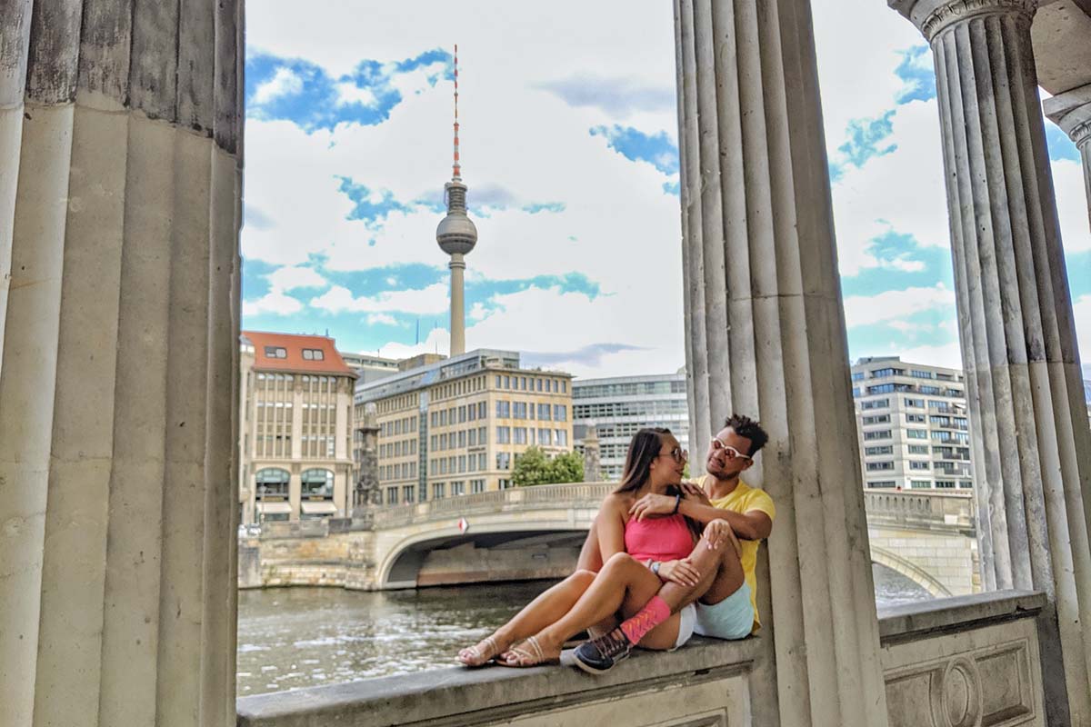 a couple seated on a ledge between stone columns at Museum Island, reflecting on the cost of living in Berlin