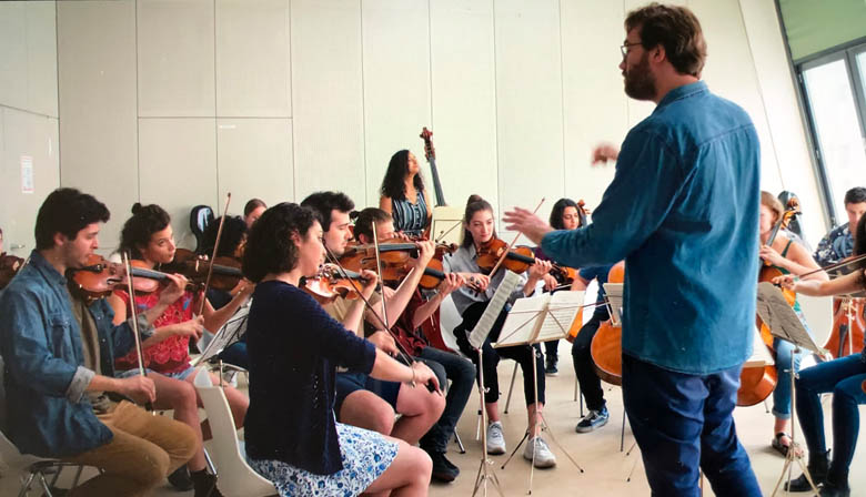 conductor orchestrating a live orchestra scene from unorthodox netflix