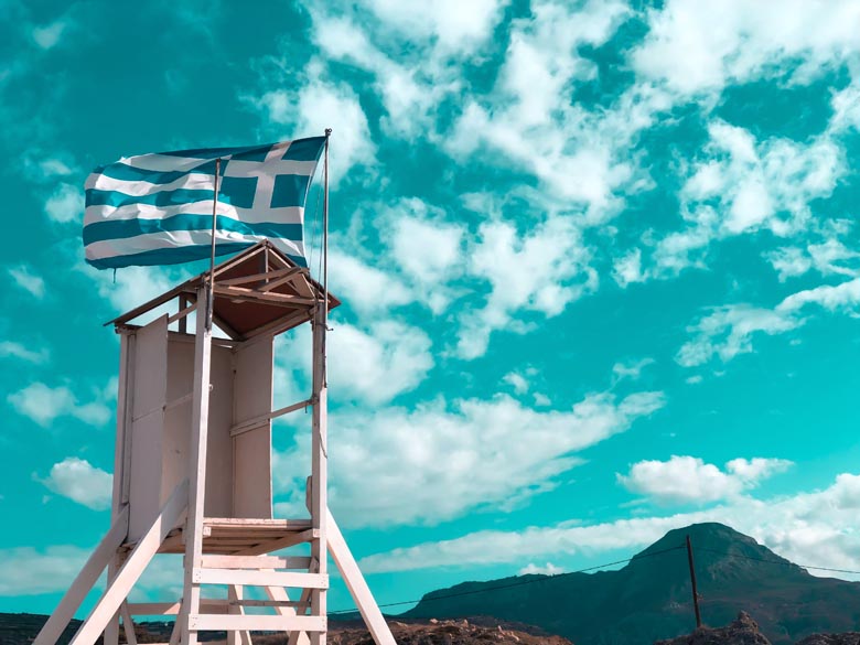 a white wooden lifeguard post on the beach with a greek flag waving in the wind