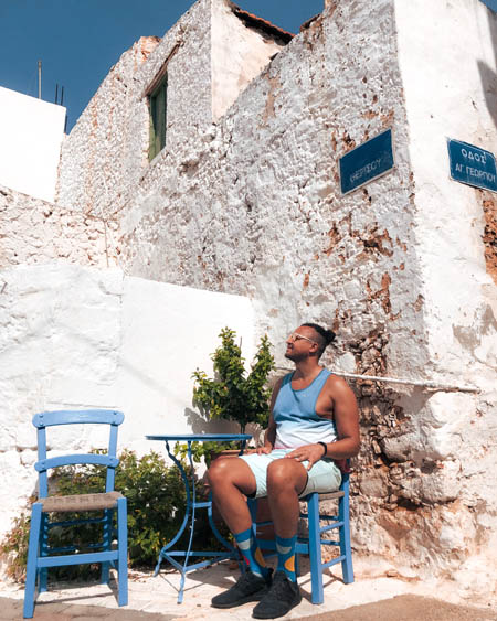a man sitting on a blue chair in the charming streets of old town malia against blue and white architecture in crete