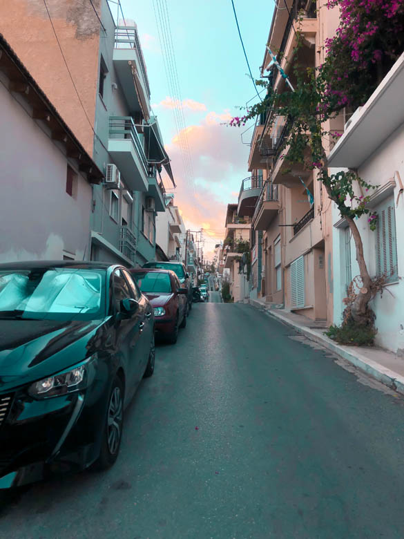 a narrow road in agios nikolaos in crete with cars parked along the side of the road