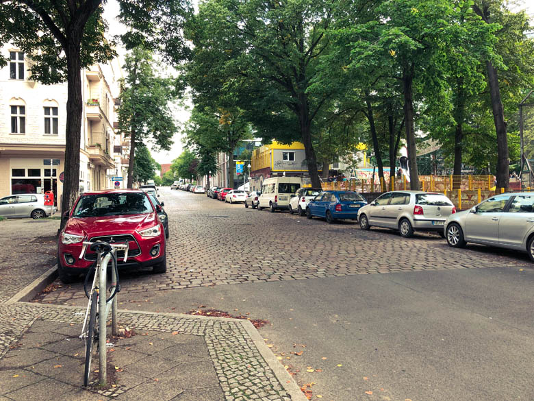 a cobble stone road in berlin with cars parked on either side and a bicycle parked on the sidewalk