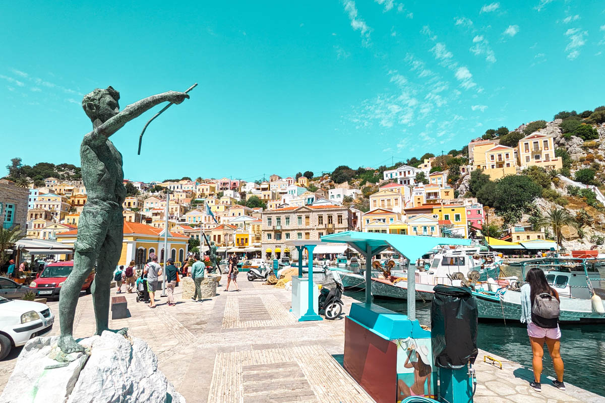 the colorful harbor of symi island near rhodes with a statue of a boy pointing towards the aegean sea