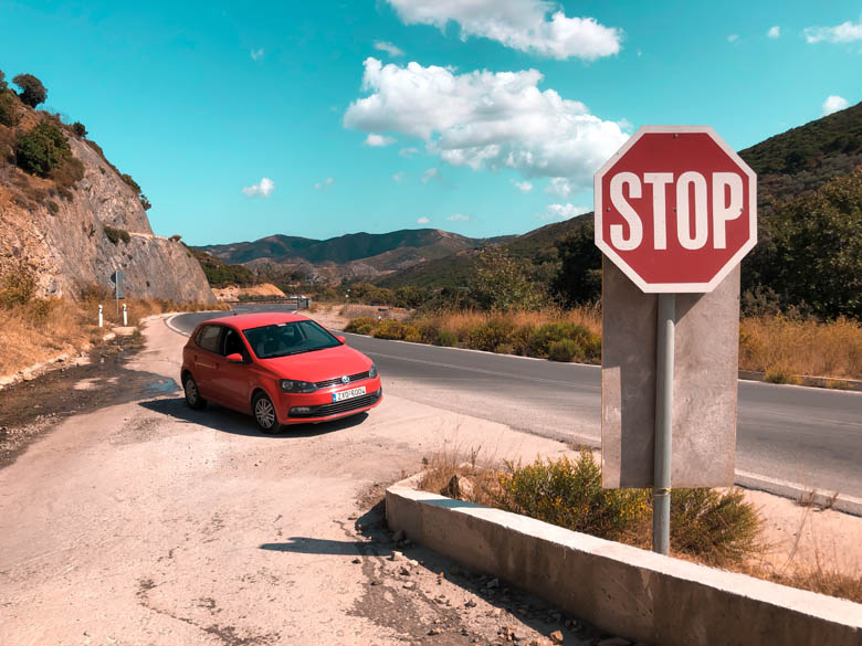 a red vw polo car hire parked on the side of the road next to a stop sign 