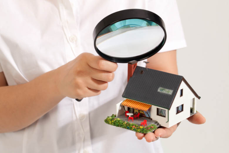 a person holding a magnifying glass inspecting a small model of a home