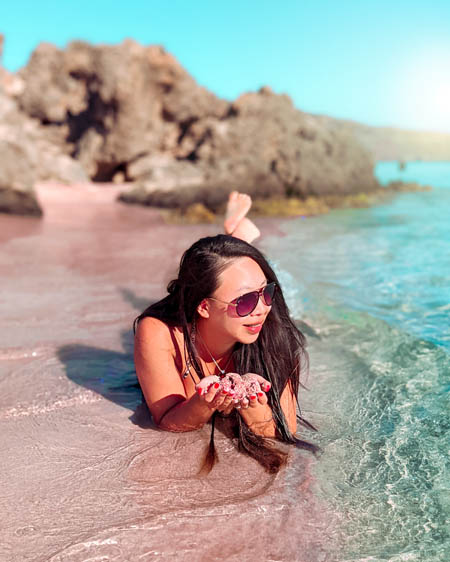 a woman lying on the pink sand at elafonissi beach in crete greece as turquoise blue waters laps the shore