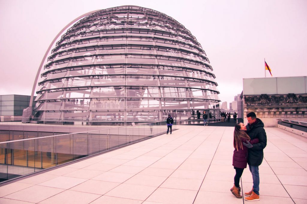 an expat couple standing on the roof of reichstag parlimentary building in berlin with glass dome in the background