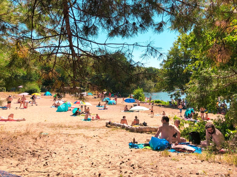 lots of people sitting on a sandy beach at flakensee lake near berlin