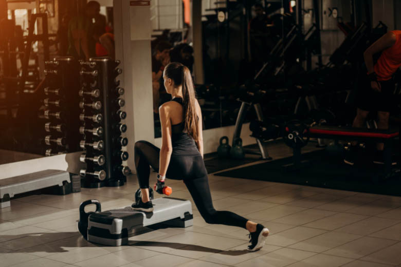 a woman doing lunges on a step at a gym with weights in her hands