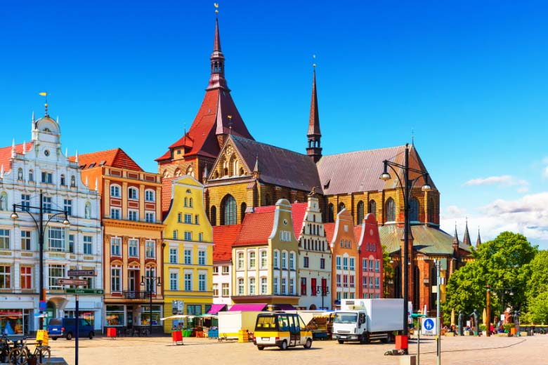 a row of colorful buildings in iconic German-style architecture in front of a church with a steeple in the background