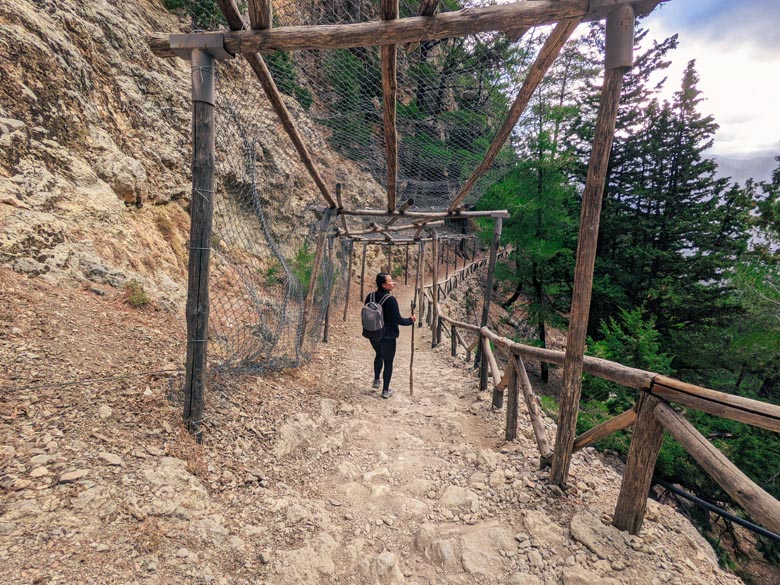 a woman hiking samaria gorge with an overhead fence canopy above providing protection against falling rocks