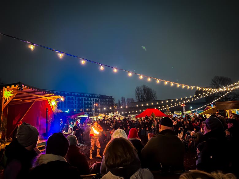 people crowding around a man performing a fire show at the historical christmas market in friedrichshain berlin