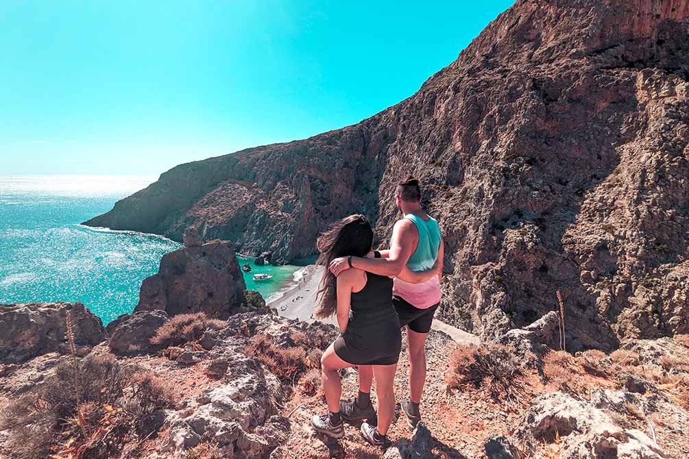 a couple standing with a view of a beautiful beach in south crete sharing how expensive it is